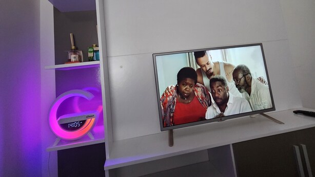 Un salon moderne avec un téléviseur à écran plat posé sur un meuble blanc, une horloge néon et une étagère sur laquelle se trouve un produit en coton.