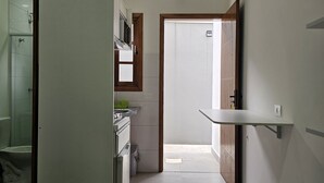 Une chambre d’hôtel compacte comprenant un coin cuisine, une zone douche et un lit avec une couvre-lit à motifs.