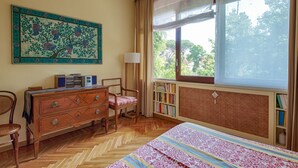 A room with a bed, a wooden dresser, a chair, a bookshelf, and a large window with a view of trees. - Parioli Luxury Terrace (Roma)