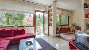 A modern living room with a red sofa, a glass coffee table, a flat-screen TV, and a bookshelf. - Parioli Luxury Terrace (Roma)