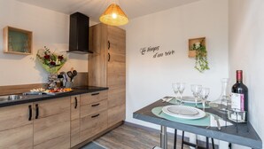 Een moderne keuken met houten kastjes, een eettafel gedekt met wijnglazen, en een muur met een Franse tekst.