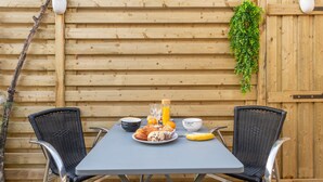 Een houten hek met twee planten in potten, een tafel met stoelen en een ontbijt met croissants, sinaasappelsap en een banaan.