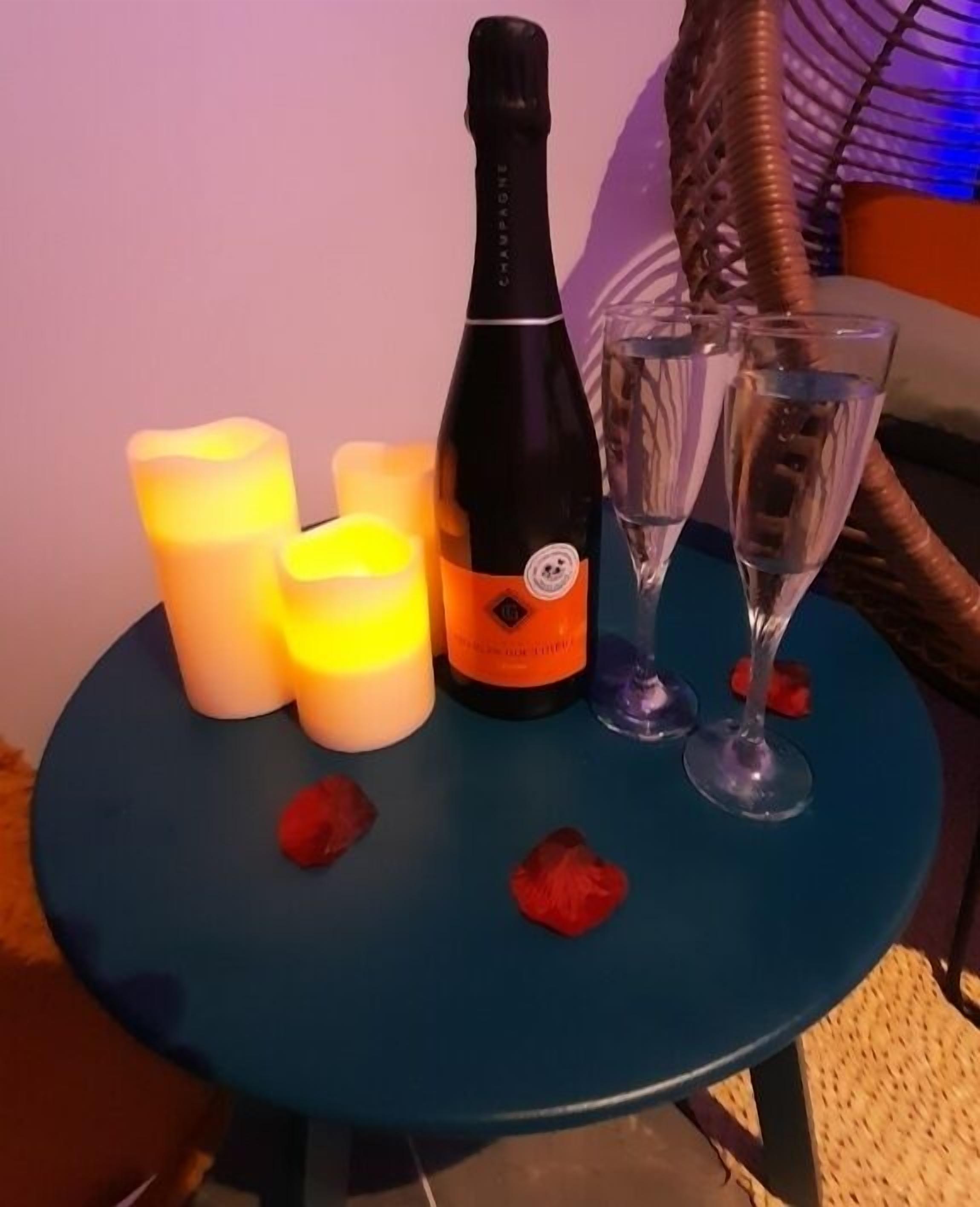 Una tavola con una bottiglia di champagne, due bicchieri e candele accese.