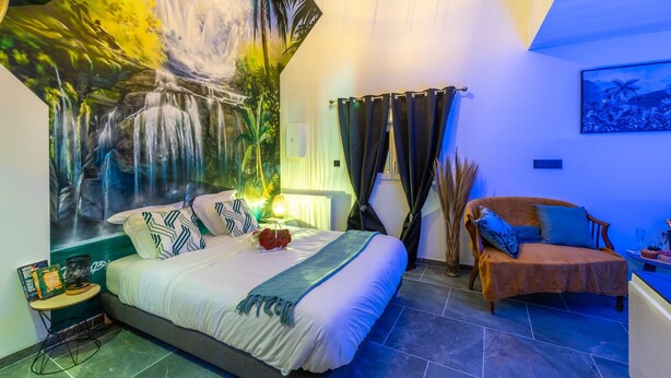 Ein Schlafzimmer mit einem Bett, einem Nachttisch, einem Sessel, einem Wandbild und einem Gemälde.