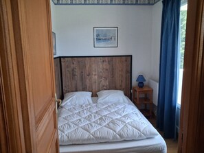 A bed with a wooden headboard, a small bedside table with a lamp, and a framed picture on the wall. - Les Oursons - Station de ski accessible à pied (La Bresse)