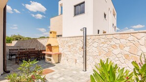 A modern villa with a stone wall, outdoor seating, and a built-in oven.