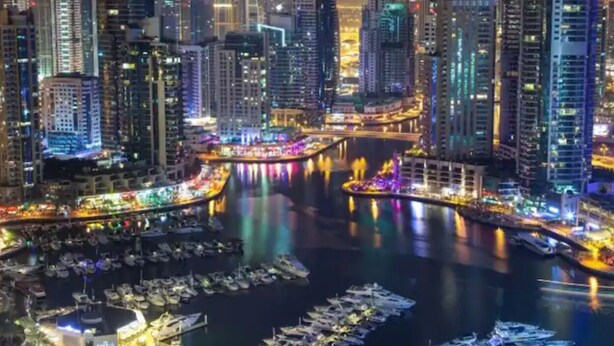 A nighttime cityscape with illuminated skyscrapers and a marina with boats. - Russian Beach  JBR (Dubai)