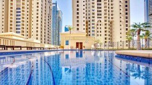 A swimming pool with clear blue tiles, surrounded by high-rise buildings and palm trees. - Russian Beach  JBR (Dubai)