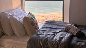 A bed with white and colorful pillows, a gray blanket, and a rolled towel. - Russian Beach  JBR (Dubai)
