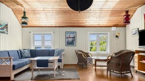 A cozy room with a wooden ceiling, a blue sofa, wicker chairs, and a table.