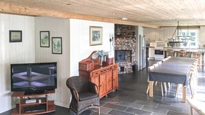 A spacious living area with a television, wicker furniture, a brick fireplace, and a kitchen in the background.