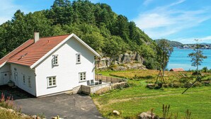 A white house with a red roof, a porch, and a view of a lake and forest.
