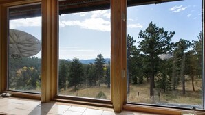 Ein Zimmer mit großen Fenstern und Blick auf einen bewaldeten Hang und Berge.