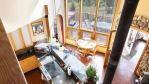 Eine moderne Küche mit einer großen Kochinsel, einem Essbereich mit Tisch und Stühlen sowie einem Blick ins Freie durch große Fenster.
