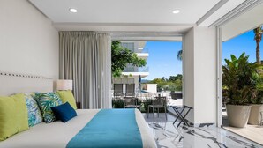 A modern hotel room with a large bed, a balcony with outdoor seating, and a view of the cityscape. - Quinta San Miguel alberca y playa 5 min (Nuevo Nayarit)