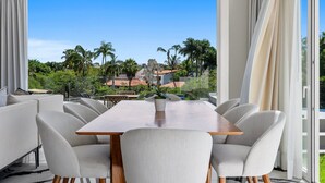 A dining area with a large table and chairs, a view of a building with palm trees, and a clear sky. - Quinta San Miguel alberca y playa 5 min (Nuevo Nayarit)