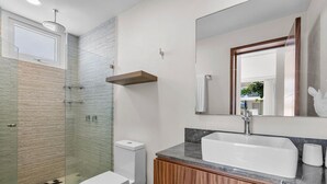 A modern bathroom with a glass shower enclosure, a white toilet, a vanity with a sink, and a mirror. - Quinta San Miguel alberca y playa 5 min (Nuevo Nayarit)