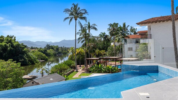 A swimming pool with a view of a river and mountains, surrounded by palm trees and a building with a tiled roof. - Quinta San Miguel alberca y playa 5 min (Nuevo Nayarit)