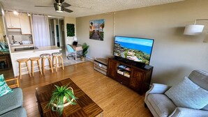 Uma sala de estar com uma mesa de centro de madeira, sofá, televisão e uma área de cozinha com conjunto de jantar.