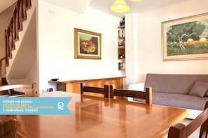 A dining area with a wooden table and chairs, a sofa, a staircase, and a bookshelf with books. - VIVA2 - Numana, four-room apartment in villa with swimming pool (Numana)