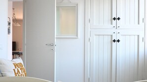 Una puerta blanca con un ventanal pequeño, un armario blanco con pomos negros y una pared blanca con una lámpara.