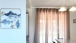 Una habitación con una mesa de comedor, un ventanal con cortinas y una decoración de peces en la pared.