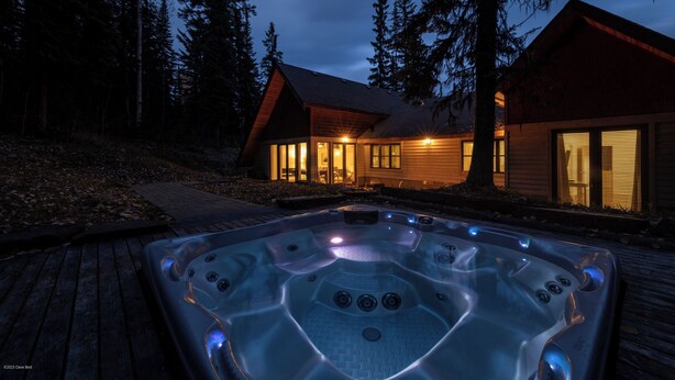 A wooden cabin with a hot tub in front, surrounded by trees.