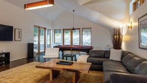 A spacious living room with a pool table, leather sofa, and a flat-screen TV.