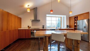 A modern kitchen with wooden cabinets, a stainless steel refrigerator, and a large window providing a view of trees.