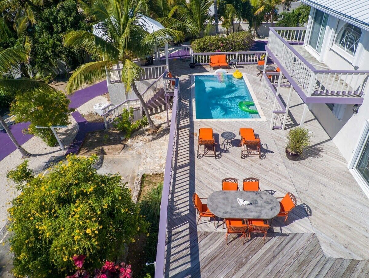 A rooftop pool area with a wooden deck, orange outdoor furniture, and a view of the surrounding landscape.