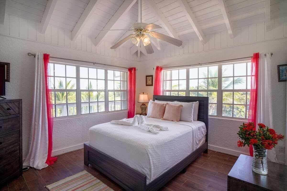A bedroom with a bed, a nightstand, a dresser, and a window with curtains.