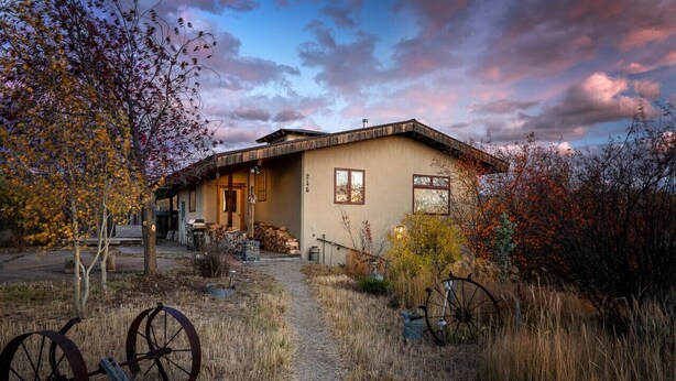Una casa rustica con un sentiero sterrato che conduce all'ingresso, circondata da foglie autunnali e un cielo sereno.
