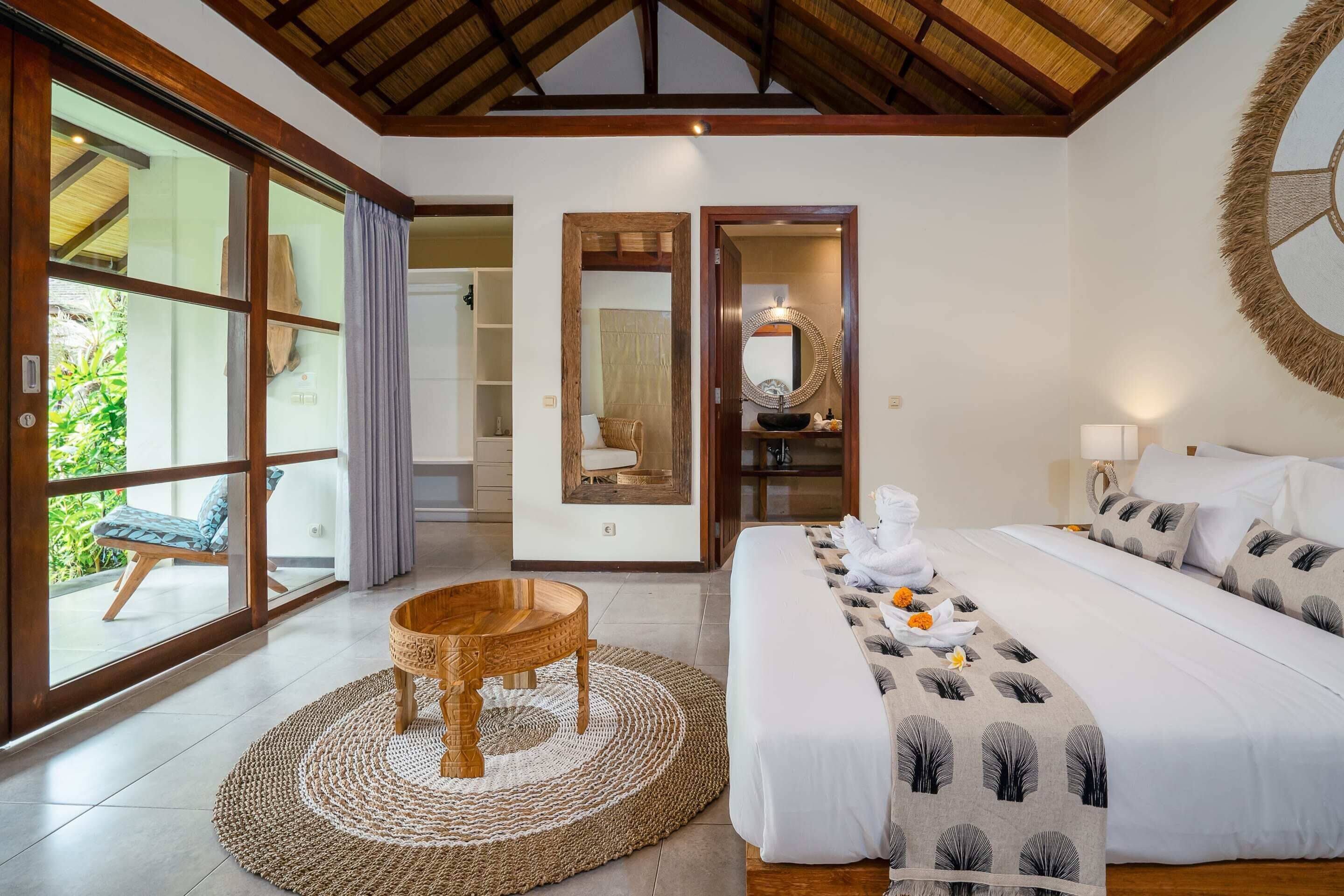 Quarto espaçoso com uma cama grande, uma mesinha de madeira e vista para área externa através de uma porta de vidro.