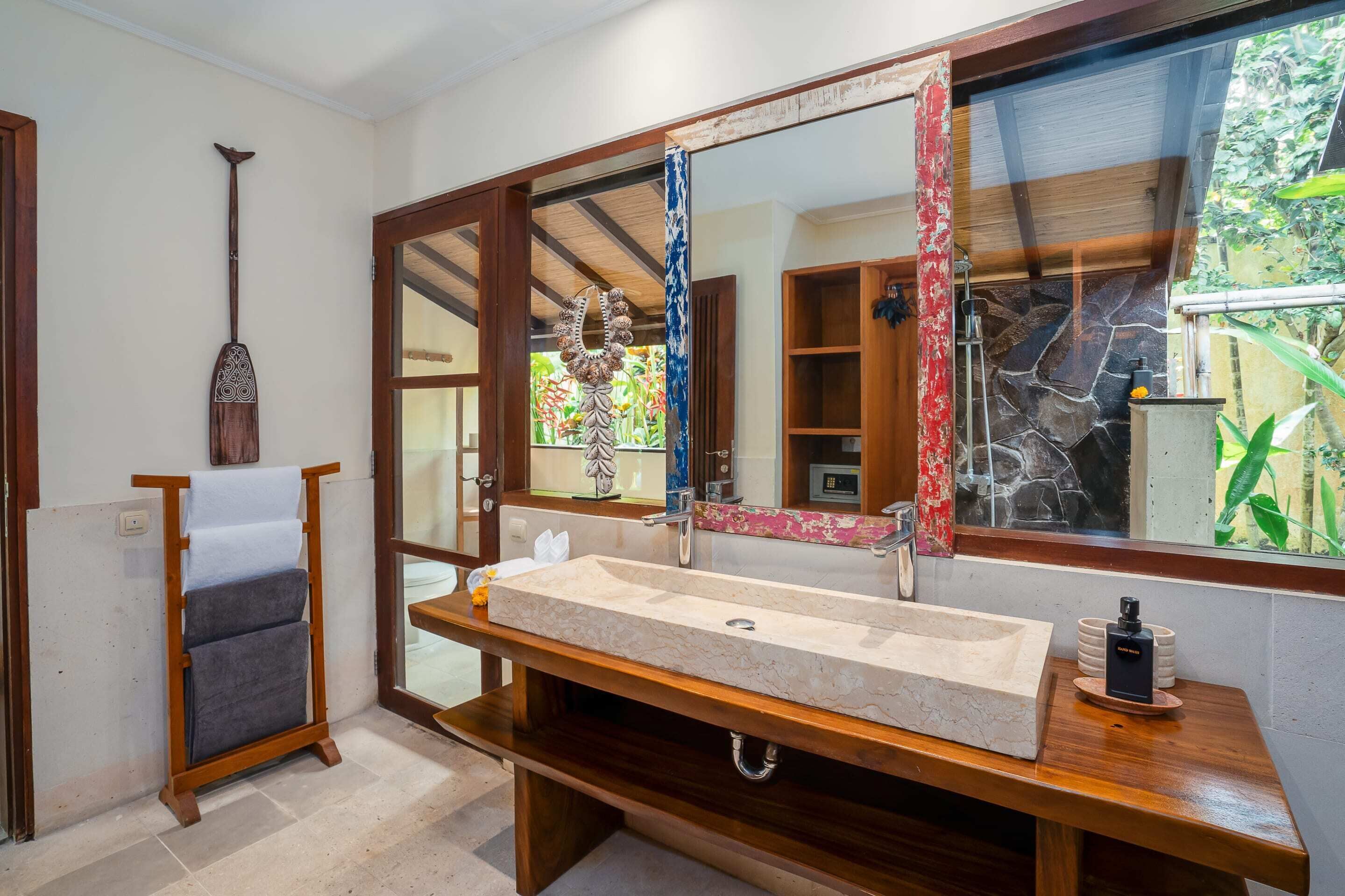 A bathroom with a large mirror, wooden vanity, and a stone sink.
