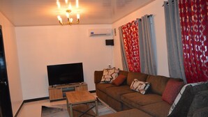 A living room with a flat-screen TV, a wooden coffee table, a brown sofa, and patterned cushions. - Cozy 2-bedroom apartment in central location with WiFi, AC (Demerara-Mahaica)
