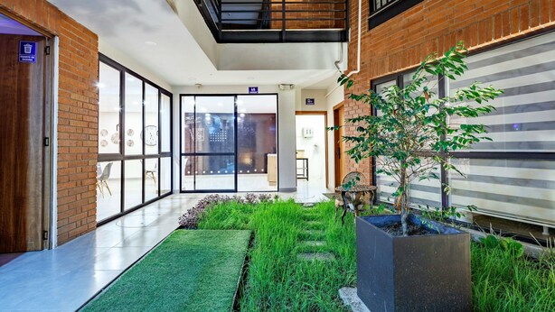 A modern hotel corridor with a brick wall, glass doors, a small indoor garden, and a staircase.