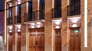 A two-story building with a brick facade, large wooden doors, and balconies with metal railings.
