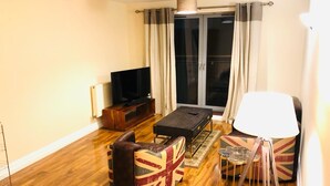 Una sala de estar con una televisión de pantalla plana, un sofá, una mesa de centro y una lámpara.