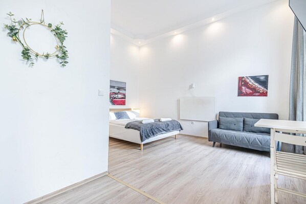 A modern bedroom with a bed, a gray sofa, a white desk, and two paintings on the wall.