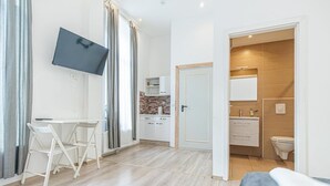 A modern apartment with a dining area, a TV mounted on the wall, a kitchen, and a bathroom.