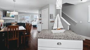 A modern kitchen with a granite countertop, white cabinetry, and a dining area with wooden chairs.