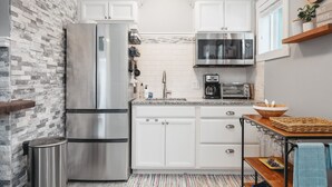 A kitchen with white cabinets, a stainless steel refrigerator, a microwave, and a toaster. - Studio TC Close to Downtown Beaches and Wineries (Traverse City)