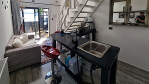 A modern kitchen with a built-in sink, a dining area with a red chair, and a staircase leading to an upper level.