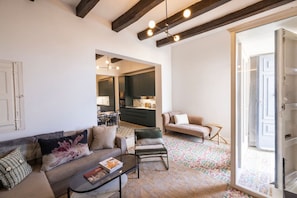 Un salon moderne avec un canapé, un fauteuil et une table basse, un coin cuisine et un sol à motifs.