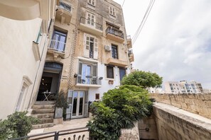 Ein mehrstöckiges Gebäude mit Balkonen, einer Treppe zum Eingang und einer kleinen Außen-Sitzgelegenheit.