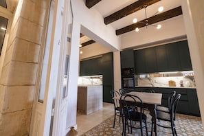A modern kitchen with dark cabinets, a marble countertop, and a dining area with a table and chairs. - Harbour Mansion 2 bedroom Maisonette (Birgu)