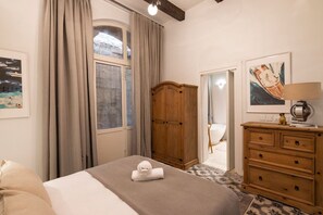 Ein Hotelzimmer mit einem Bett, einem Holzschrank, einem Schreibtisch mit Lampe und einem fenster mit Vorhängen.