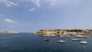 Una marina costera con barcos amarrados, un edificio histórico fortificado y cielos despejados.