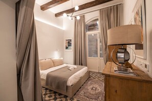 A bedroom with a bed, a desk, a lamp, and a window with curtains. - Harbour Mansion 2 bedroom Maisonette (Birgu)