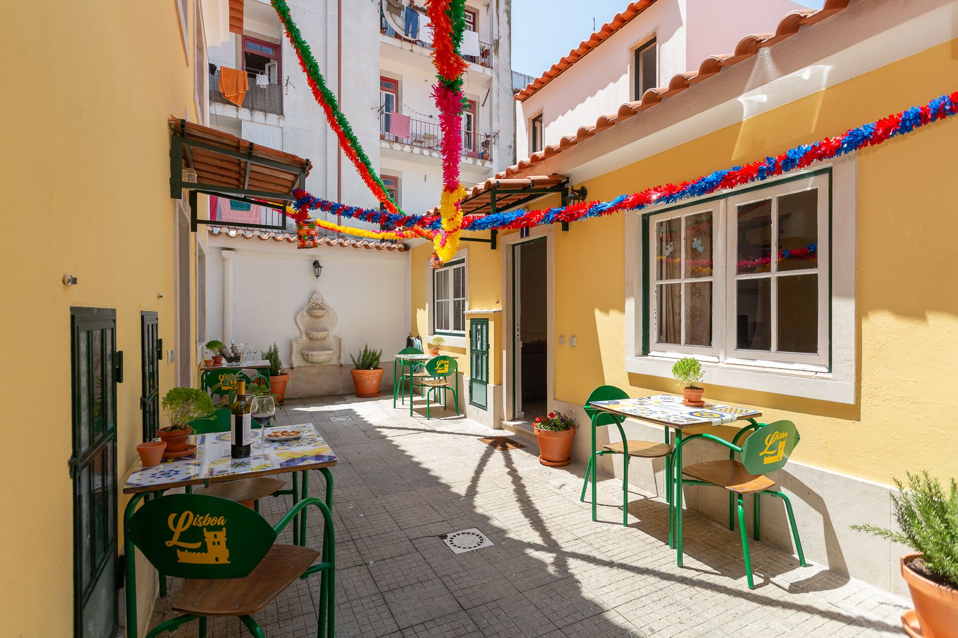 A narrow outdoor patio with tables and chairs, decorated with colorful garlands.